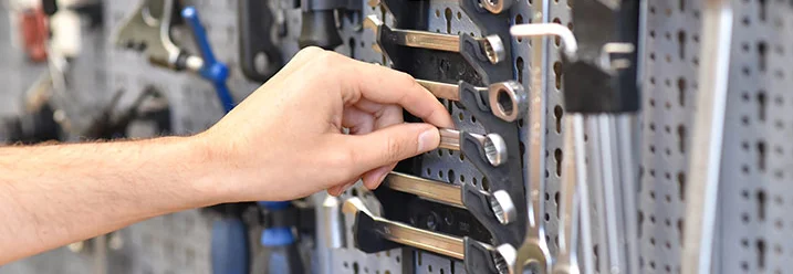 Eine Hand greift nach einem Schraubenschlüssel an einer Werkzeugwand.